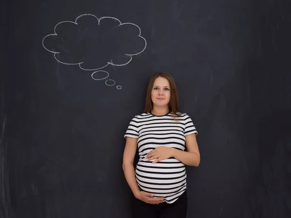 young pregnant woman thinking about names for her unborn baby to writing them on a black chalkboard