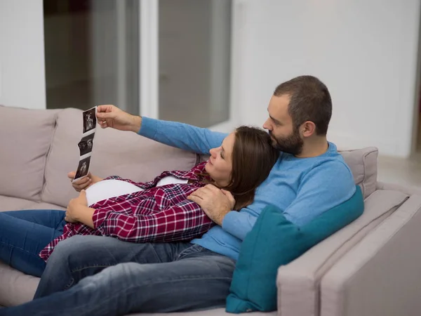 Young Pregnant Couple Looking Baby Ultrasound Photo While Relaxing Sofa — Stock Photo, Image