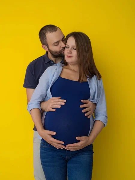 一对快乐的年轻夫妇的肖像 男子抱着他怀孕的妻子腹部孤立的黄色背景 — 图库照片