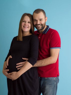 Mutlu genç bir çift hamile eşi karnı tutan adam portresi üzerinde mavi arka plan izole