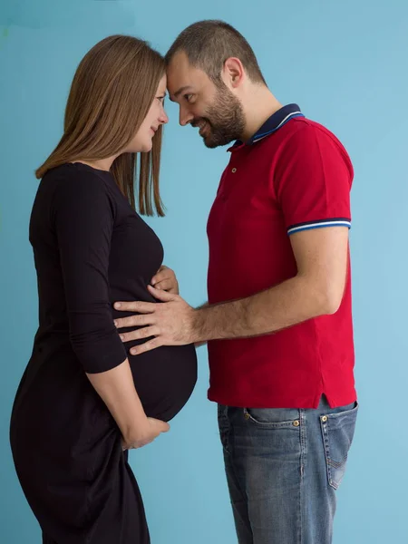 一对快乐的年轻夫妇的肖像 男子抱着他怀孕的妻子腹部孤立的蓝色背景 — 图库照片