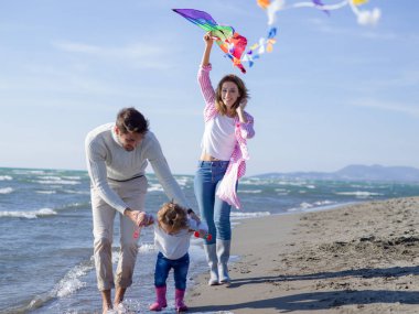 Küçük kızının dinlendiği ve sonbahar günü kumsalda uçurtmayla eğlendiği bir aile.