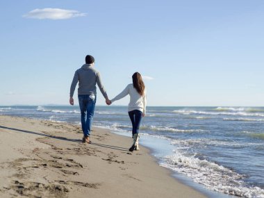 Young couple having fun walking and hugging on beach during autumn sunny day clipart