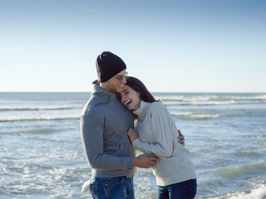 Genç çift, sonbahar güneşli bir günde kumsalda yürüyüp sarılıyor.