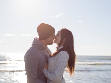 Genç çift, sonbahar güneşli bir günde kumsalda yürüyüp sarılıyor.