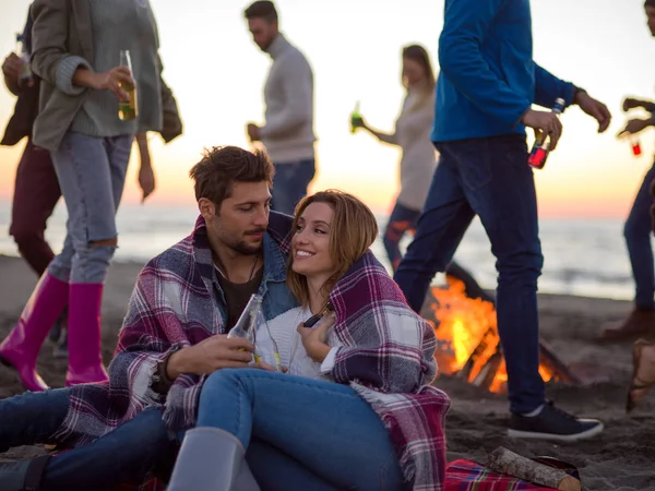 在日落时分和朋友们一起坐在海滩篝火边喝啤酒 — 图库照片