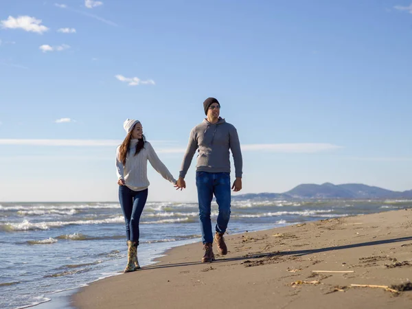 Genç çift, sonbahar güneşli bir günde kumsalda yürüyüp sarılıyor.