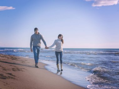 Genç çift, sonbahar güneşli günlerinde kumsalda yürüyüp sarılıyor. Renkli filtre.