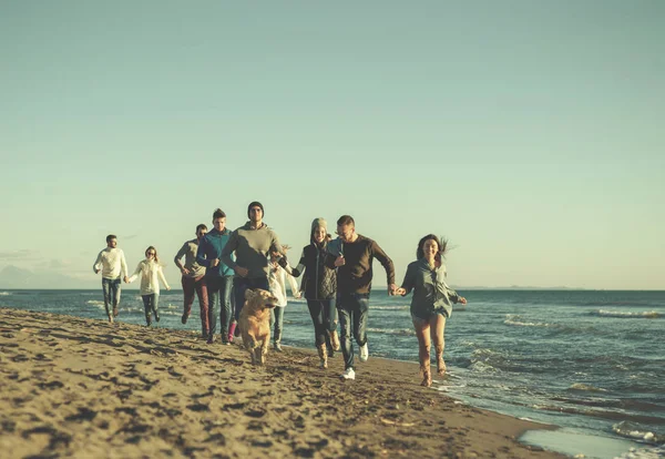 一群年轻的朋友在秋天的时候一起在海滩上跑来跑去 — 图库照片