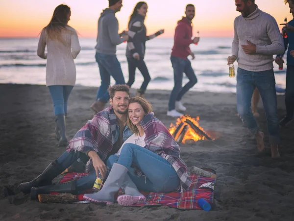 在日落时分 与朋友坐在海滩篝火边 喝着啤酒 喝着彩色滤水器 — 图库照片