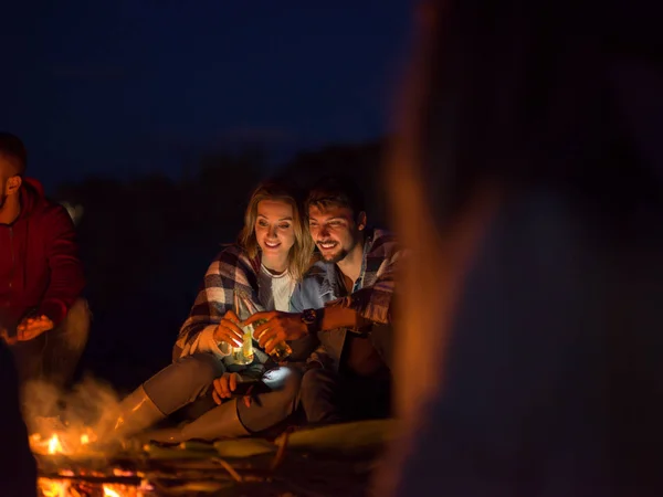 Pareja Joven Sentada Con Amigos Alrededor Campfire Playa Por Noche —  Fotos de Stock