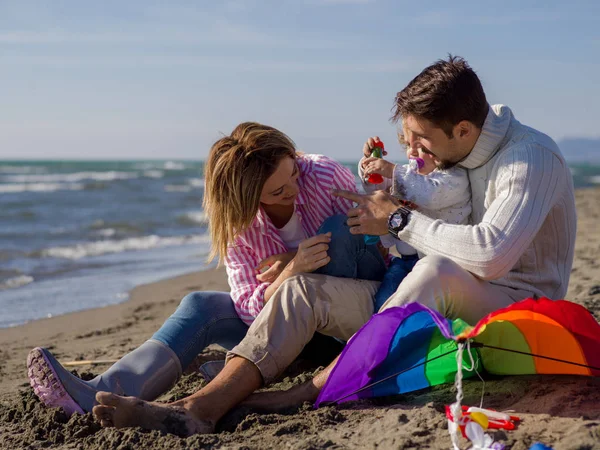 Küçük kızının dinlendiği ve sonbahar günü kumsalda uçurtmayla eğlendiği bir aile.