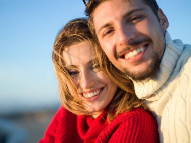 Sonbahar güneşli bir günde sahilde eğlenen genç bir çiftin portresi.