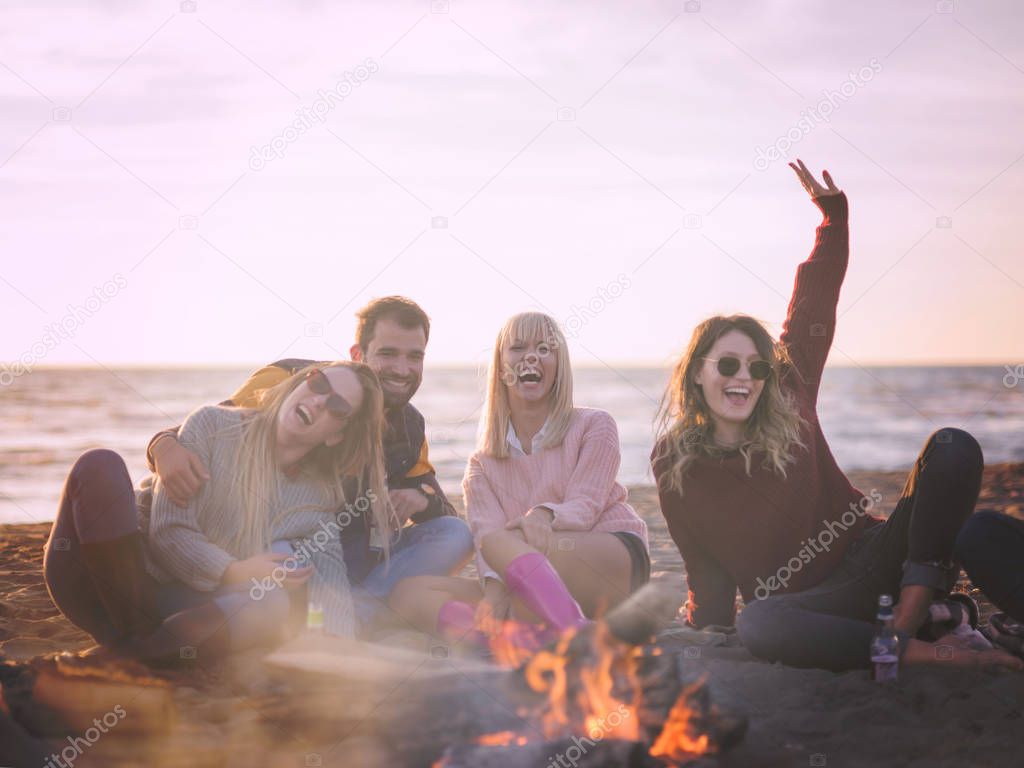 Happy Carefree Young Friends Having Fun And Drinking Beer By Bonefire On The Beach As The Sun Begins To Set colored filter