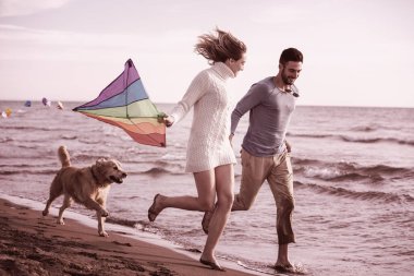 Genç çift eğlenmek bir köpek ve sonbahar günü plaj uçurtma ile oynarken