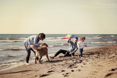 Mutlu ve çocuklu bir aile sonbahar günü filtresi boyunca sahilde köpek ve uçurtmayla eğleniyor.