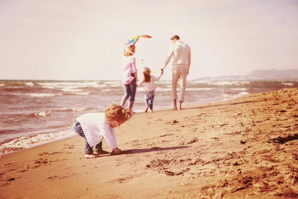 秋の日のフィルターの間にビーチでカイトと休んで楽しんでいる子供たちを持つ若い家族 — ストック写真