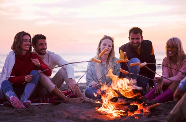 一群年轻的朋友坐在秋天海滩的篝火边 烤香肠 喝啤酒 玩乐地过滤 — 图库照片