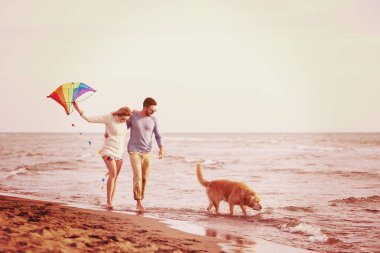 Genç çift eğlenmek bir köpek ve sonbahar günü plaj uçurtma ile oynarken