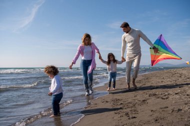 Genç bir aile, çocukları dinleniyor ve sonbahar günü kumsalda uçurtmayla eğleniyorlar.