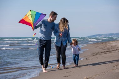 Genç bir aile, çocukları dinleniyor ve sonbahar günü kumsalda uçurtmayla eğleniyorlar.