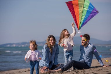 Genç bir aile, çocukları dinleniyor ve sonbahar günü kumsalda uçurtmayla eğleniyorlar.