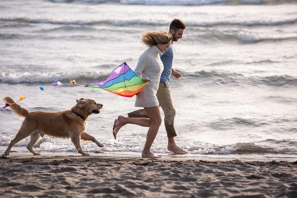 若いカップルが楽しんで犬 秋の日にビーチにカイトで遊んで — ストック写真