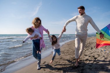 Genç bir aile, çocukları dinleniyor ve sonbahar günü kumsalda uçurtmayla eğleniyorlar.