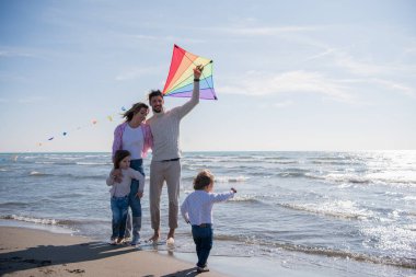 Genç bir aile, çocukları dinleniyor ve sonbahar günü kumsalda uçurtmayla eğleniyorlar.