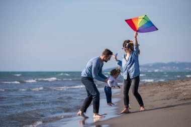 Genç bir aile, çocukları dinleniyor ve sonbahar günü kumsalda uçurtmayla eğleniyorlar.