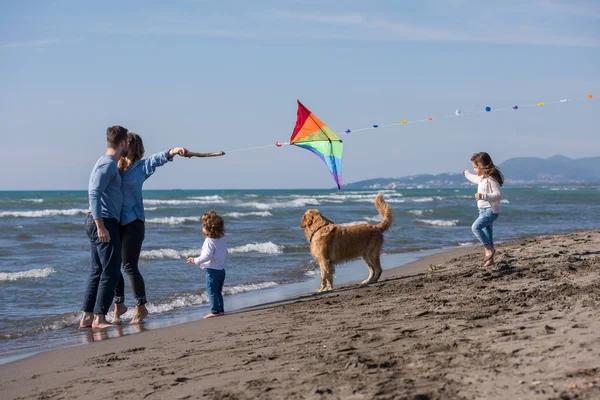 Mutlu ve çocuklu bir aile sonbahar günü sahilde köpek ve uçurtmayla eğleniyor.
