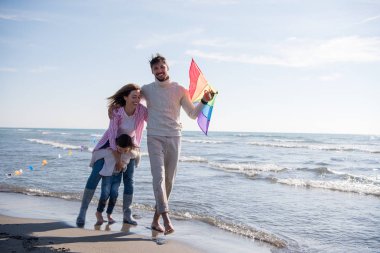 Genç bir aile, çocukları dinleniyor ve sonbahar günü kumsalda uçurtmayla eğleniyorlar.