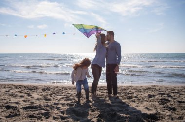 Genç bir aile, çocukları dinleniyor ve sonbahar günü kumsalda uçurtmayla eğleniyorlar.