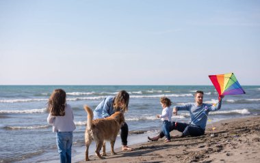 Mutlu ve çocuklu bir aile sonbahar günü sahilde köpek ve uçurtmayla eğleniyor.