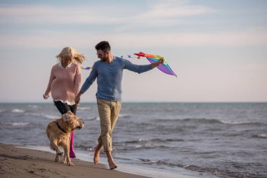 Genç çift eğlenmek bir köpek ve sonbahar günü plaj uçurtma ile oynarken