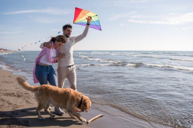 Genç çift eğlenmek bir köpek ve sonbahar günü plaj uçurtma ile oynarken