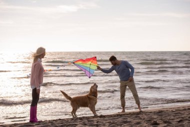 Genç çift eğlenmek bir köpek ve sonbahar günü plaj uçurtma ile oynarken