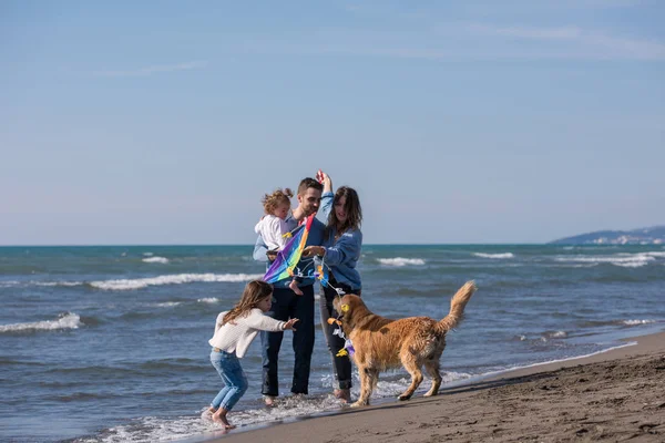 秋の日にビーチで犬と凧を楽しんでいる子供たちと幸せな若い家族 — ストック写真