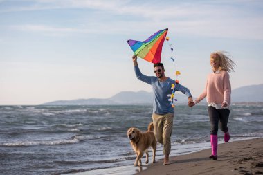 Genç çift eğlenmek bir köpek ve sonbahar günü plaj uçurtma ile oynarken