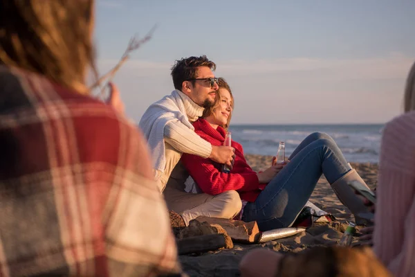 在日落时分 年轻夫妇和朋友们一起在海滩篝火边畅饮啤酒 — 图库照片