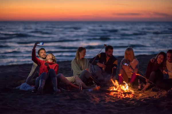 Grupp Vänner Som Använder Mobiltelefoner Runt Brasan Höstens Strandparty Dricker — Stockfoto