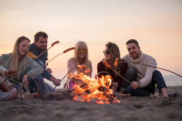 Grupo Jóvenes Amigos Sentados Junto Fuego Playa Otoño Asando Salchichas —  Fotos de Stock