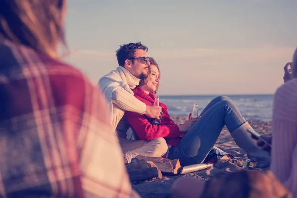 在日落时分 年轻夫妇和朋友们一起在海滩篝火边畅饮啤酒 — 图库照片