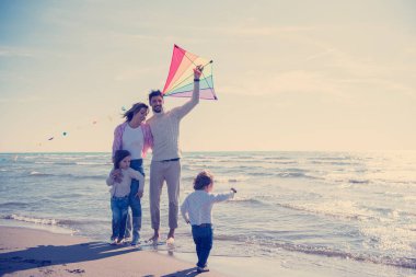 Genç bir aile, çocukları dinleniyor ve sonbahar günü kumsalda uçurtmayla eğleniyorlar.