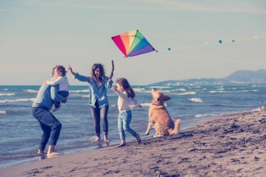 Mutlu ve çocuklu bir aile sonbahar günü sahilde köpek ve uçurtmayla eğleniyor.