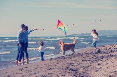 Mutlu ve çocuklu bir aile sonbahar günü sahilde köpek ve uçurtmayla eğleniyor.