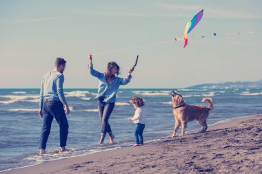 Mutlu ve çocuklu bir aile sonbahar günü sahilde köpek ve uçurtmayla eğleniyor.