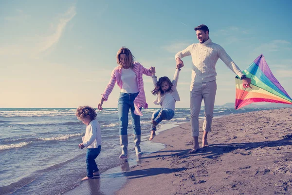 Genç bir aile, çocukları dinleniyor ve sonbahar günü kumsalda uçurtmayla eğleniyorlar.