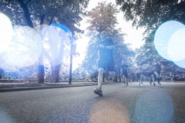 Bir grup sağlıklı insan şehir parkında koşuyor, koşucular sabah antrenmanında.