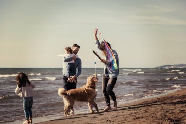 Mutlu ve çocuklu bir aile sonbahar günü filtresi boyunca sahilde köpek ve uçurtmayla eğleniyor.
